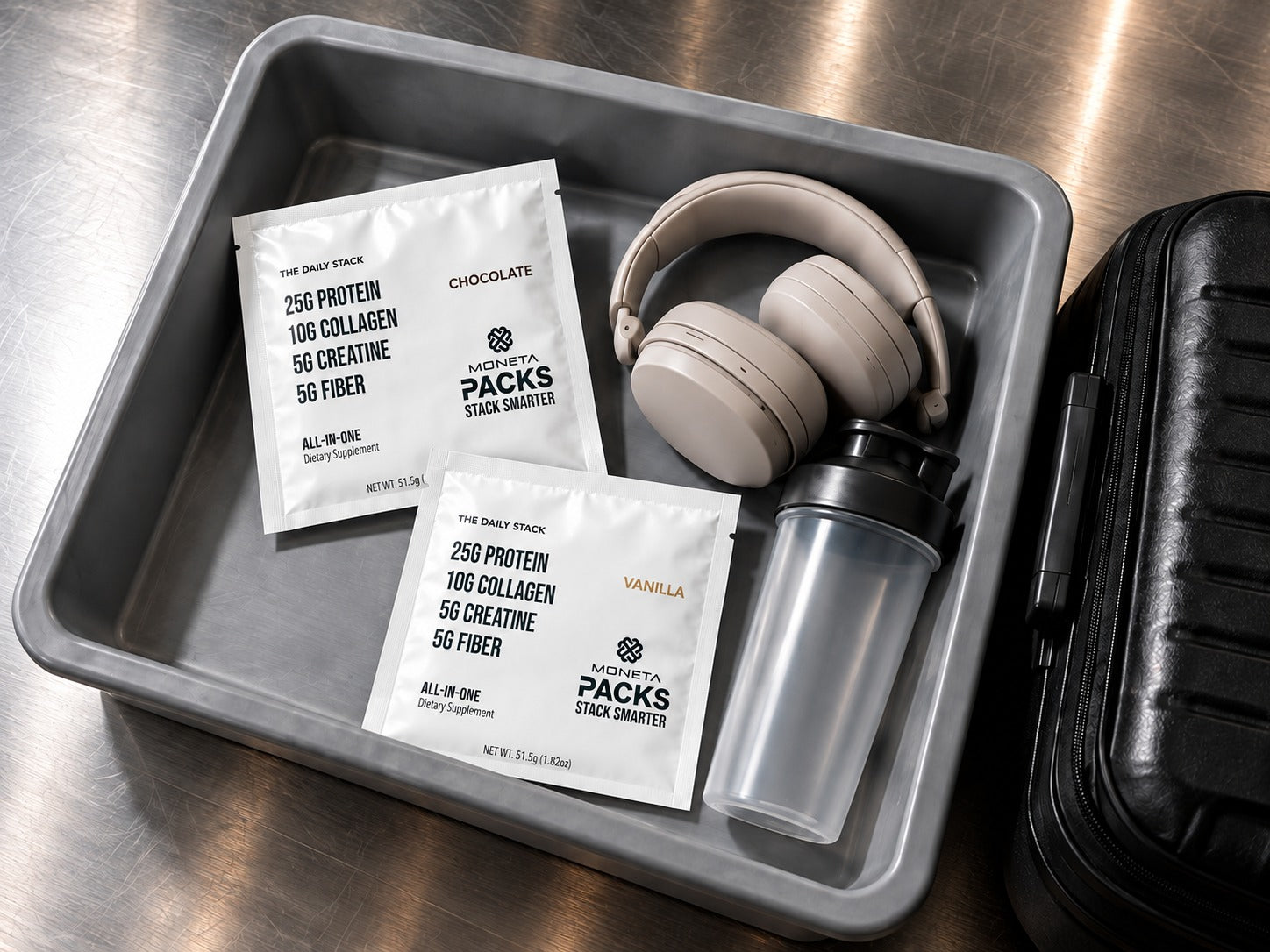 Moneta PACKS packed beside headphones and a shaker in an airport tray