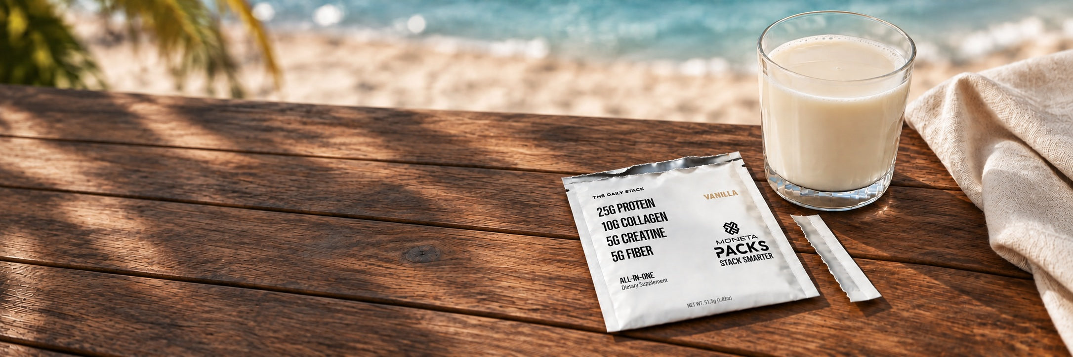 A prepared vanilla drink beside an opened Moneta PACK on a beachside table